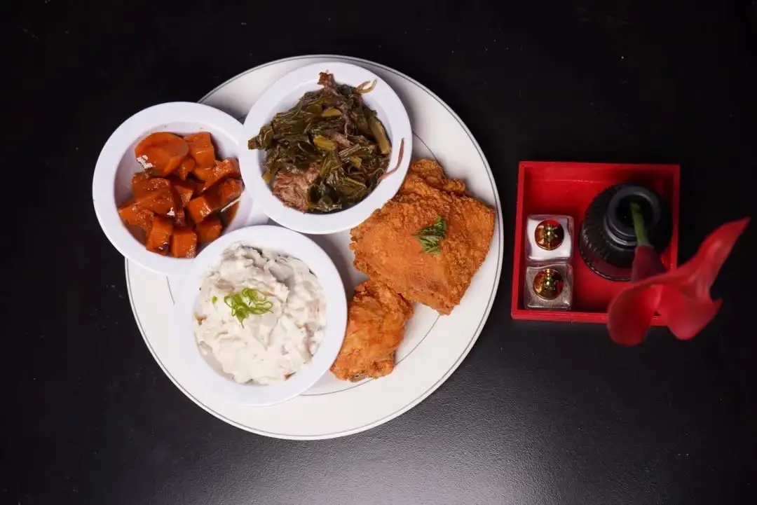A Soul Food on 68 plate of crispy fried chicken with candied yams, collard greens, and potato salad